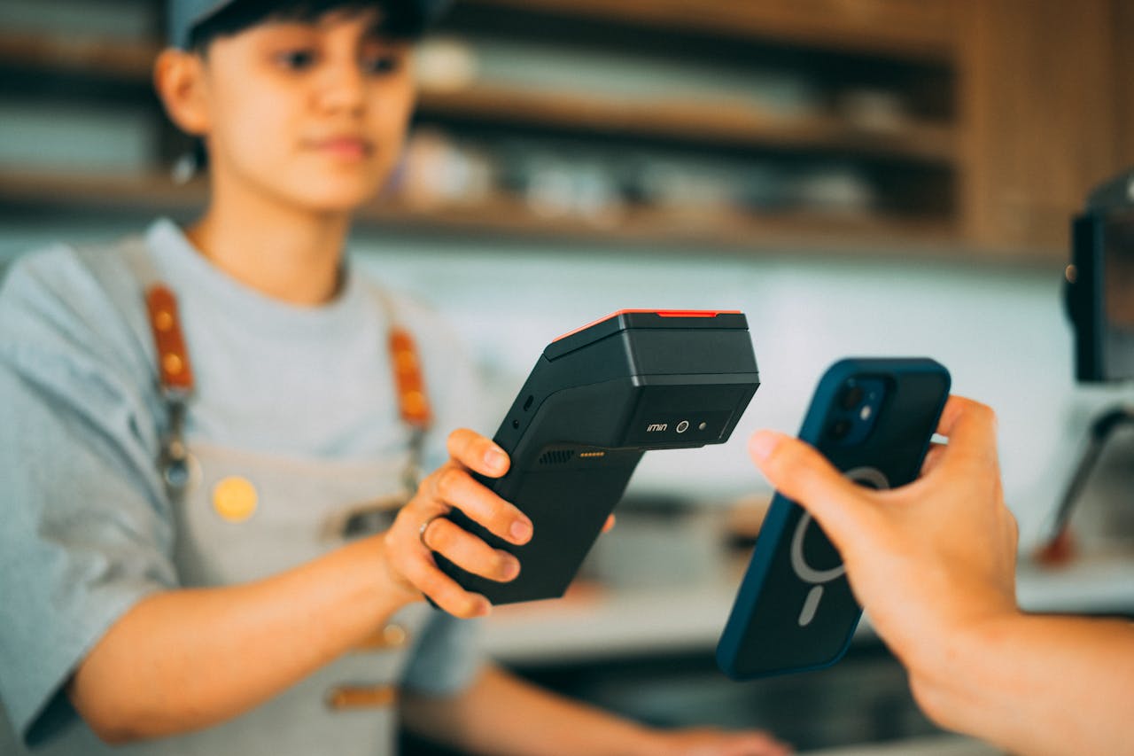 A cashier processes a contactless payment using a smartphone and card reader.